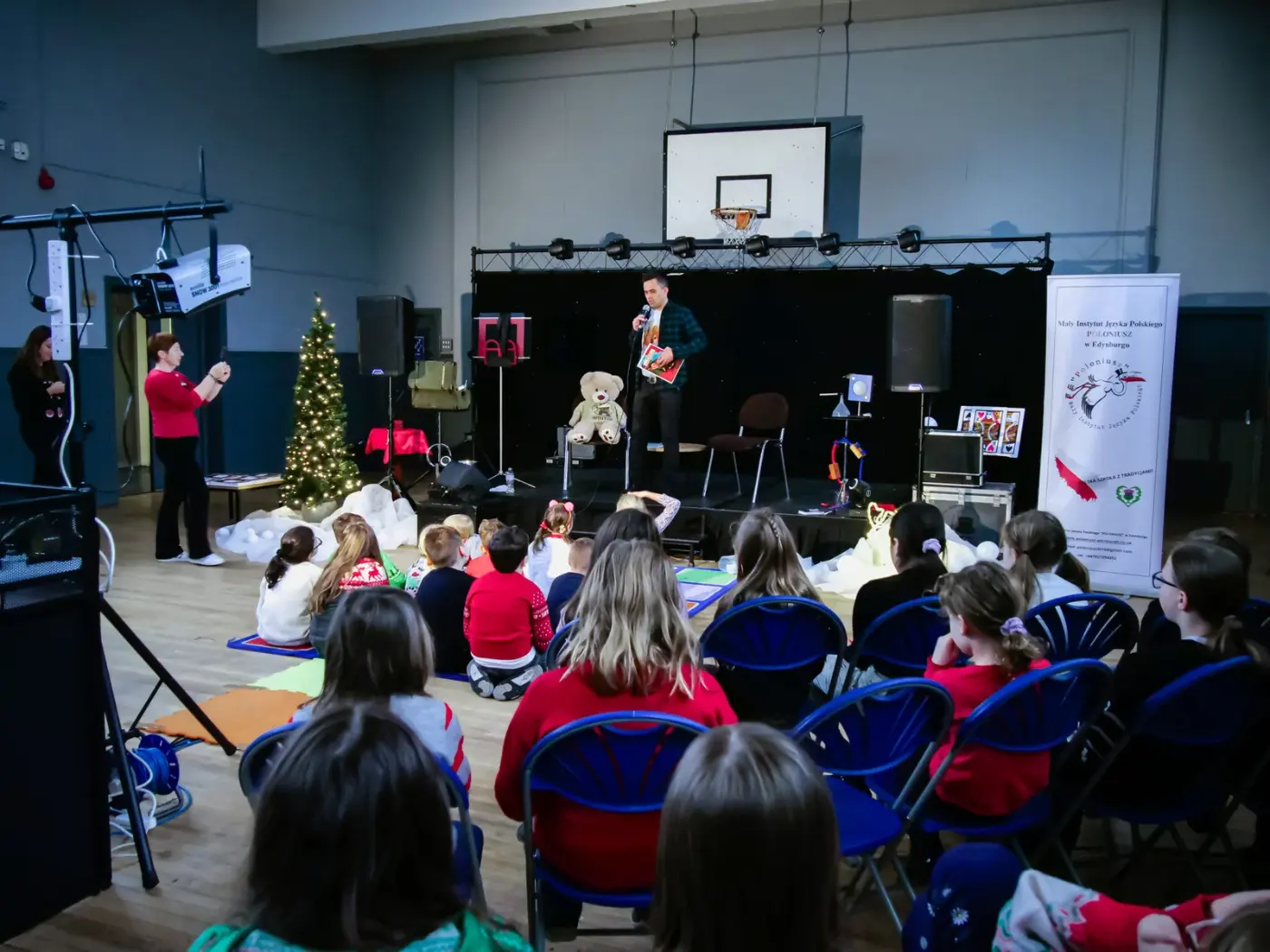 Wojciech Filaber reading to an audience of children beside a large teddy bear